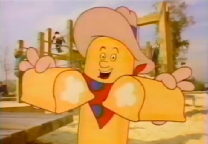 A cartoon character shaped like a snack cake, wearing a cowboy hat and bandana, smiles while holding two pieces of a snack cake. The background features a playground with climbing structures and a child playing.