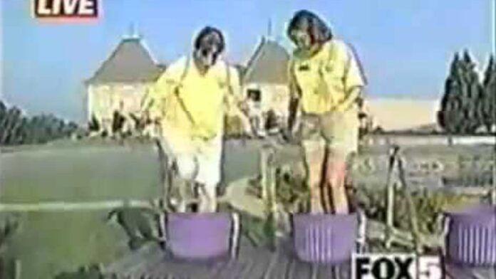 Grape Stomp Viral Video Still - Two people in yellow shirts are stepping into purple containers outdoors. A LIVE label is in the top left corner, and a FOX 5 logo is at the bottom right. A building with pointed roofs is in the background.