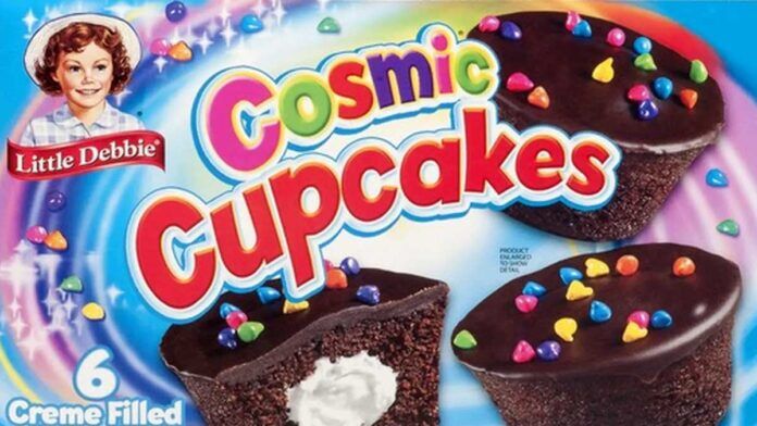 A box of Little Debbie Cosmic Cupcakes, showing chocolate cupcakes with colorful candy toppings and a creme-filled center. The packaging features a retro-style image of a smiling young girl.